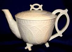 a white ceramic tea pot with a handle on it's side and an ornate design around the top