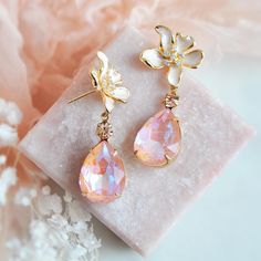 Add a dash of electric sparkle with these gorgeous flower earrings! The organic flowing flower earring posts are created with off white enamel and accented with tiny cubic zirconia. Secured to the flowers are shimmering faceted peachy pink teardrops set inside of vintage raw brass bezels which have a warm patina finish adding to their vintage charm. Embellished to the teardrops are tiny faceted champagne colored crystals for added sparkle. Whether adding these peach pink earrings for a lovely to Pink Drop Flower Earrings For Formal Occasions, Feminine Crystal Drop Earrings For Wedding, Feminine Teardrop Wedding Earrings, Pink Formal Flower Drop Earrings, Pink Teardrop Flower Earrings For Wedding, Pink Teardrop Pearl Earrings For Wedding, Pink Teardrop Wedding Earrings, Pink Feminine Pearl Earrings For Wedding, Feminine Pink Pearl Earrings For Wedding