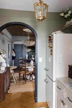 an arched doorway leads to a dining room and kitchen area with white cabinets, wood flooring and gold accents