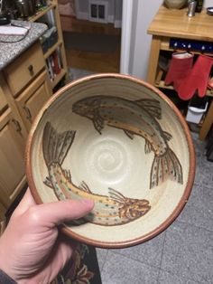 a person holding up a bowl with fish on it in a room full of wooden cabinets