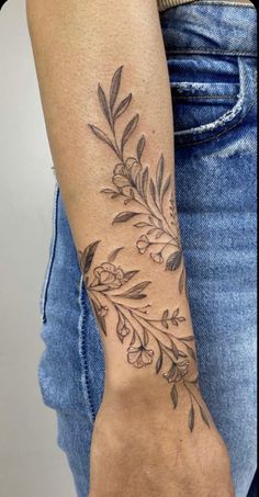 a woman's arm with a tattoo on it that has leaves and flowers on it