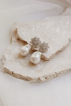 two white pearls are sitting on a piece of lace next to a brooch pin