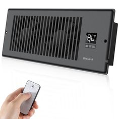 a person holding a remote control in front of a wall mounted air conditioner with an alarm clock on it