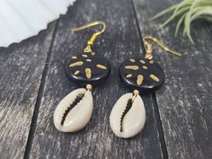 "These gorgeous dangle earrings feature genuine off-white sliced moneta cowrie shells dangling beneath 20mm round carved black and gold acrylic beads an etched Afrocentric abstract pattern. Aching for acrylics? Check out the rest of my acrylic jewelry here: https://etsy.me/2IadiWZ Throughout Africa and the Americas, cowrie shells have historically been viewed as symbols of womanhood, fertility, and prosperity. Check out my other cowrie shell jewelry here: https://etsy.me/2VQS0r0 These earrings m Cowrie Shell Earrings For Gifts, Black Dangle Jewelry For Beach, Black Drop Earrings For Summer, Artisan Black Jewelry For The Beach, Black Shell Jewelry For Gifts, Black Shell Jewelry Gift, Black Shell Jewelry As A Gift, Unique Black Beach Jewelry, Handmade Black Jewelry For Vacation