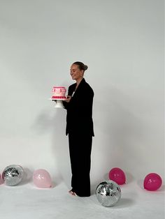 a woman holding a cake in front of balloons