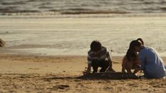 two people and a dog are sitting on the sand at the beach near the water