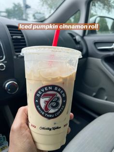 a person holding up a cup of iced pumpkin cinnamon roll in their hand and steering wheel behind the car