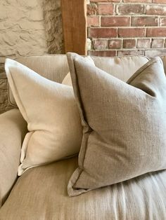 two pillows sitting on top of a couch next to a brick wall