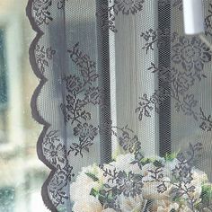 a vase with flowers sitting on a window sill in front of a lace curtain