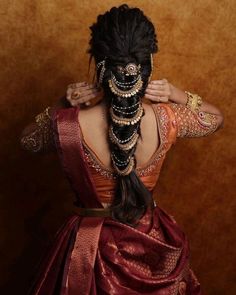 a woman with long black hair wearing a red and gold saree, holding her hands behind her head