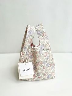 a small floral bag with a tag hanging from it's front pocket on a white surface