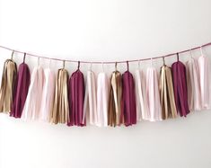 several tassels hanging from a string on a white wall with pink and gold colors