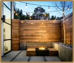 an outdoor fire pit in the middle of a patio with string lights strung over it