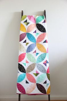 a colorful quilt hanging on a wall next to a wooden stand with an ironing board