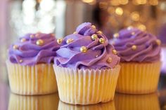 three cupcakes with purple frosting and gold sprinkles on them