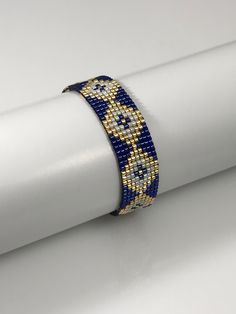 a blue and gold bracelet sitting on top of a white piece of cloth next to a roll of paper