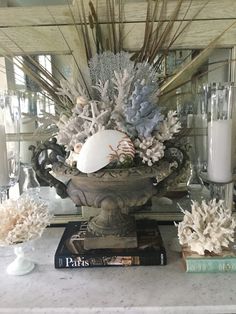 a vase filled with sea shells sitting on top of a table next to candles and books