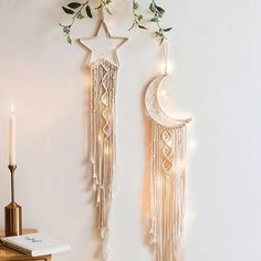 two wall hangings decorated with lights and greenery next to a candle on a table