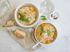 two bowls filled with food next to some glasses and spoons on a white table