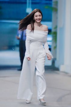 a woman in white is walking down the street with her hair blowing in the wind