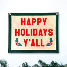 a happy holidays y'all sign hanging on the side of a building with pine branches