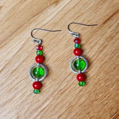 two red and green beaded earrings sitting on top of a wooden table