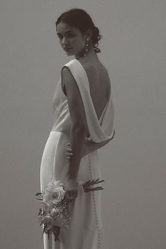 a woman in a long white dress holding a bouquet and looking off into the distance