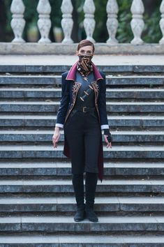 a woman standing in front of some steps wearing a mask and coat with her hands on her hips