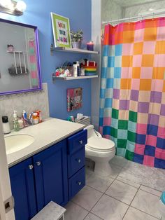 a bathroom with a colorful shower curtain next to a toilet and sink in front of a mirror