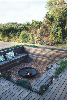 an outdoor seating area with fire pit and wooden decking, surrounded by greenery