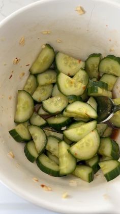 a white bowl filled with sliced cucumbers and seasoning next to a spoon