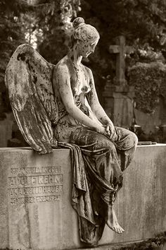 black and white photograph of an angel sitting on a stone wall in front of a cemetery