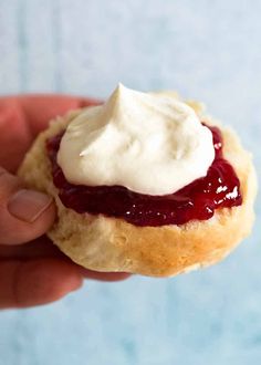 a hand holding a small pastry with cream on top and jelly in the middle,