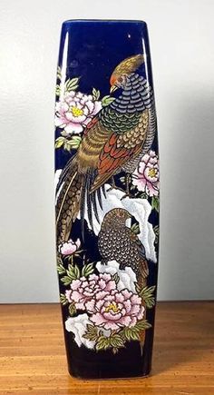 a vase with two birds on it sitting on a wooden table next to a wall