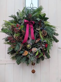 a wreath hanging on the side of a door with pine cones, evergreens and other decorations