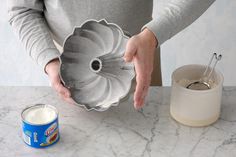 a person holding a flower shaped cake pan over a table with a can of milk next to it