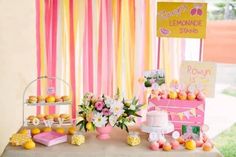 a table topped with lots of cakes and desserts next to a window covered in pink and yellow striped curtains