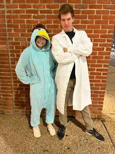 two people dressed in costumes standing next to a brick wall and posing for the camera