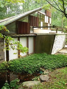 a house in the woods surrounded by trees and rocks with a stream running through it