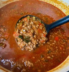 a ladle full of soup is being stirred with a wooden spoon in the bowl