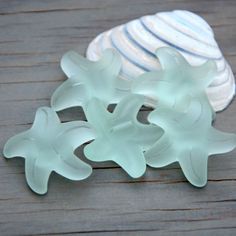 three glass pieces sitting on top of a wooden table next to a seashell and shells