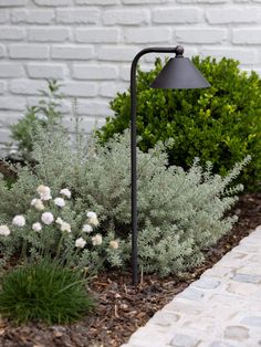 a black lamp sitting on top of a metal pole next to some bushes and flowers