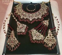 an assortment of red and gold jewelry on display in a black box with white cloth