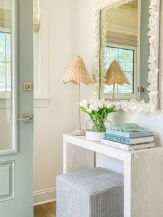 a white table topped with a vase filled with flowers next to a mirror and lamp