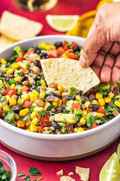 a hand dipping a tortilla chip into a bowl filled with mexican corn and black bean salsa