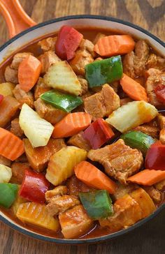 a bowl filled with meat and veggies on top of a wooden table next to an orange spoon