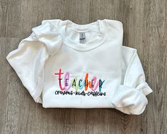 "Colorful Embroidered TEACHER Sweatshirt, Teacher Sweatshirt, Teacher Appreciation Gift for Teacher Valentine Gift, School Teacher Shirt HOW TO ORDER:  1) From the first dropdown menu, select sweatshirt size 2) From the second dropdown menu, select sweatshirt color 3) Click \"Add to Cart\" SIZING & SWEATSHIRT INFO: - Embroidery design is 5x7, the design will appear smaller on larger shirts - Larger Fit. If between sizes, we recommend sizing down - Sweatshirts are 18000 Gildan® Heavy Blend™ Adult Crewneck Sweatshirts IMPORTANT ORDERING INFORMATION: - Please review the sizing charts, with measurements, that are in the listing photos before purchasing.  CANCELLATIONS: - Cancellations are accepted within 24 hours of placing your order. After that, your order is possibly in production and we ca Long Sleeve School Tops With Embroidered Text, Casual School Tops With Embroidered Logo, Fall School Tops With Embroidered Logo, Casual Tops With Embroidered Logo For School, Fall School Tops With Embroidery, Embroidered Tops For School In Fall, Long Sleeve Sweatshirt With School Spirit Embroidery, Long Sleeve Sweatshirt With Embroidered Logo For School, Long Sleeve T-shirt With Letter Embroidery For School Spirit