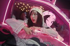 a woman sitting in the back of a pink car with an anime character on it