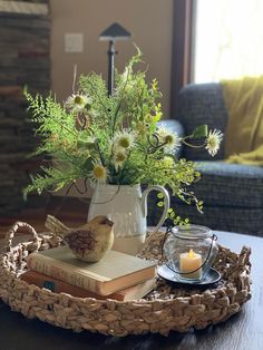 a tray with flowers, candles and books on it sitting on a table in front of a couch