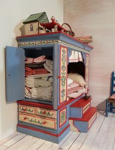 a doll house with clothes in it on top of a wooden floor next to two chairs